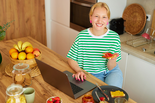 Young woman using laptop while enjoying breakfast  at home