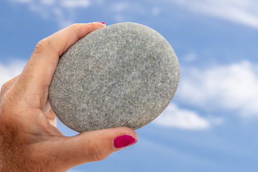 Isolated hand holding stone against a sky background.