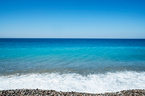 Beautiful seascape of pebble beach on sunny day with clear blue sky without clouds. Ocean view with horizon, background with a lot of copy space for text.