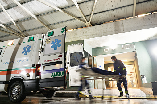 Full length view with blurred motion as male and female ambulance team transport mature woman from back of vehicle into emergency room.