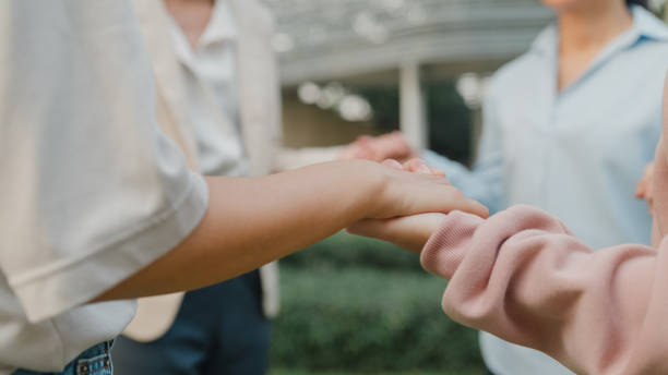 istock Closeup of group therapy session with diverse people sharing their sad problems and stories in park. Asian people group in circle hold hands together hope for help. Mental health. 1585443283