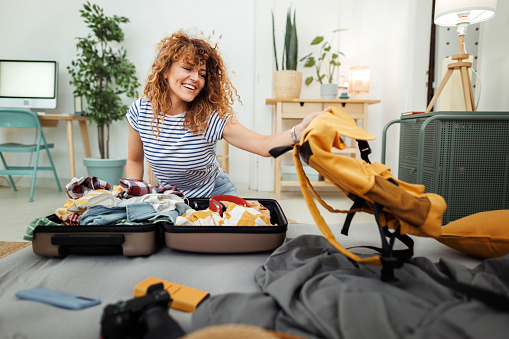 Cheerful young woman packing her suitcase for a trip at home