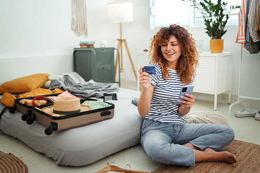 Young smiling woman making online reservation while sitting on a floor at home