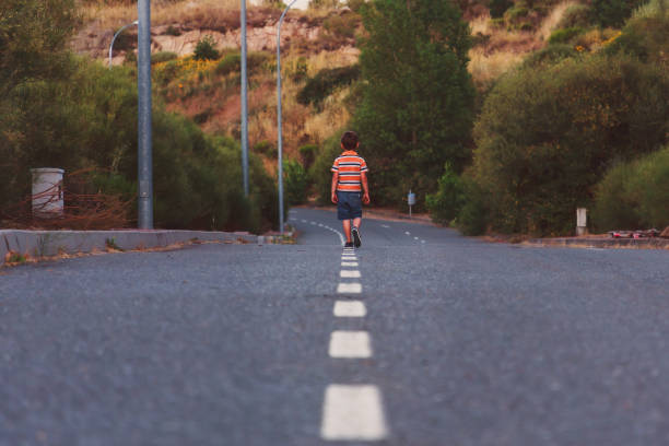 A little boy is walking along an asphalt road.