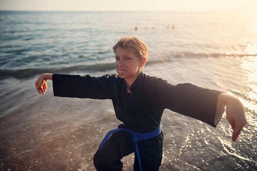 Funny fittle boy practicing kung fu on the beach.\nShow with Nikon D850