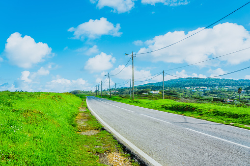 Concrete road with electric poles surrounded by green fields