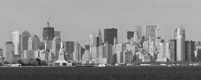 New York City lower Manhattan skyline black and white with Statue of Liberty and urban city skyline over river panorama view.