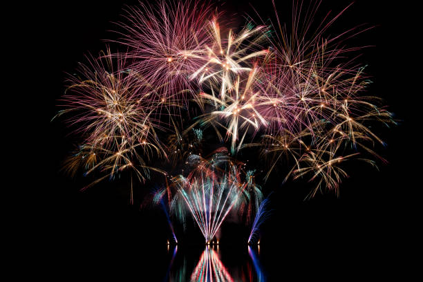 Beautiful and colorful fireworks during national holiday shot over a river with water reflections stock photo