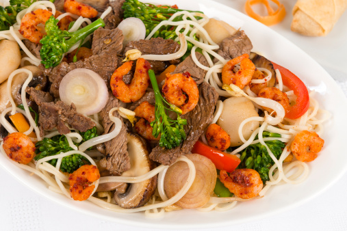 Chow mein - Chinese stir-fried noodles with beef, shrimp and vegetables on a white background. Spring rolls on the side.