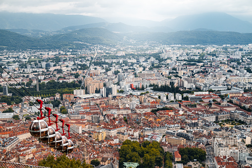 Horizontal photo of Grenoble cityscape with the famous bubble shaped, sphere, overhead Bastille cable car in foreground. This image was taken in Grenoble city on a cloudy summer day, in the department of Isere, Auvergne-Rhône-Alpes region in France, Europe.