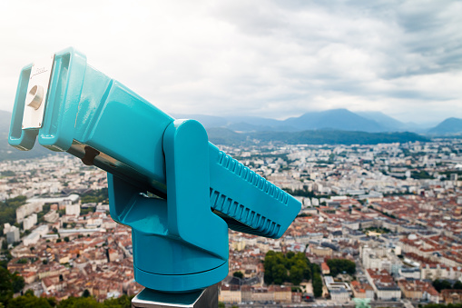Close-up of binoculars for tourists in selective focus, overlooking Grenoble city. This image was taken during a cloudy summer day, in the department of Isere, Auvergne-Rhône-Alpes region in France, Europe.