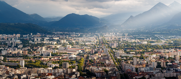 Panorama over Grenoble city at sunset, with bright sunlight through clouds during a summer day, in the department of Isere, Auvergne-Rhône-Alpes region in France, Europe.