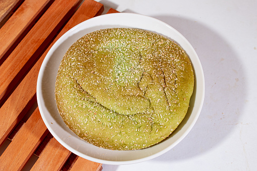 Green pandan bread with a round shape and a white plastic placemat with a plain white background and a wooden placemat