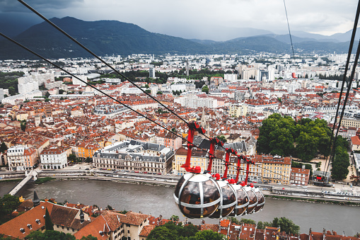 Horizontal photo of Grenoble cityscape with the famous bubble shaped, sphere, overhead Bastille cable car in foreground. This image was taken in Grenoble city on a cloudy summer day, in the department of Isere, Auvergne-Rhône-Alpes region in France, Europe.