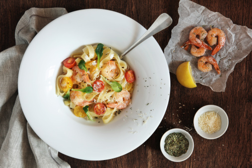Fettuccine with shrimps, cherry tomatoes and cheese sauce on wooden table.