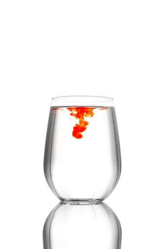 A clean glass full of water, a drop of red food coloring has just been dropped into it.