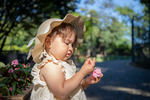 Photo of a baby girl wearing a hat and holding a flower in nature