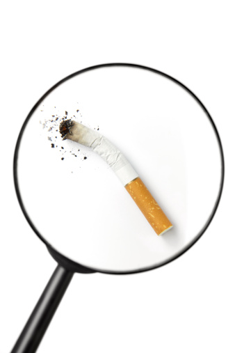 Stubbed out cigarette viewed through magnifying glass isolated on white background