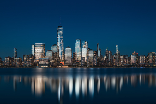 New York lower Manhattan at night shot with long exposure and reflections on Hudson River.