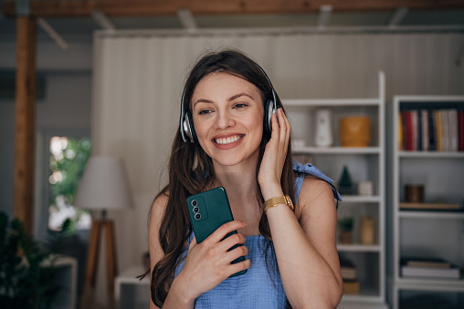 Beautiful woman listening music on headphones and using smart phone at home.