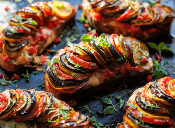 Grilled sourdough bread open faced sandwich with sliced vegetables and mozzarella cheese sprinkled with fresh herbs on a black background, close-up