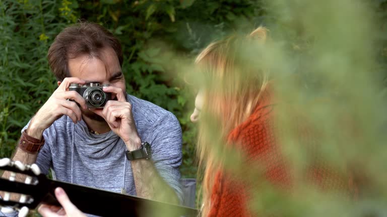 Young man taking photo of girlfriend playing guitar