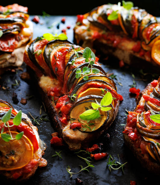 istock Grilled sourdough bread open faced sandwich with sliced vegetables and mozzarella cheese sprinkled with fresh herbs on a black background, close-up. 1585698704