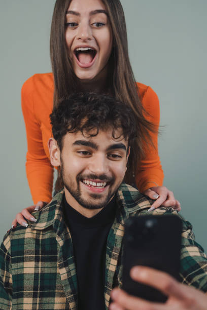 istock Young couple fun recording video stories using mobile phone isolated over grey background. Attractive beautiful girl. Streaming video. 1585705708