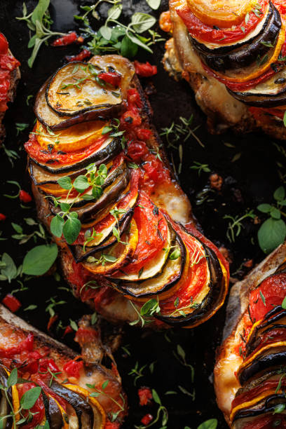 istock Grilled sourdough bread open faced sandwich with sliced vegetables and mozzarella cheese sprinkled with fresh herbs on a black background, close-up. 1585744875
