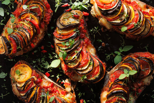istock Grilled sourdough bread open faced sandwich with sliced vegetables and mozzarella cheese sprinkled with fresh herbs on a black background, top view. 1585769520