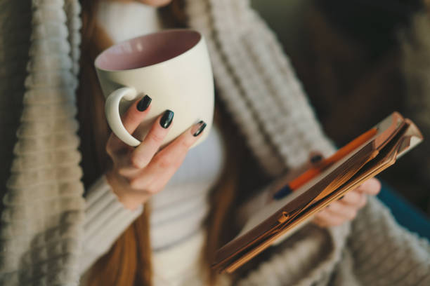 istock Close-up view of a woman's hand holding a cup and a notebook in which she writes down her thoughts. Relaxation lifestyle concept. Close-up, indoors. People lifestyle concept. 1585772369