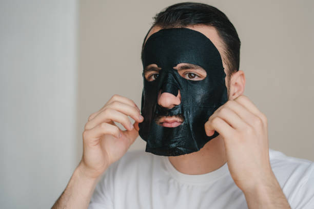Handsome man applying black face mask on his face, receiving spa treatments. Grooming himself. Facial treatment, cosmetology. Facial skin care. Perfect body. Cosmetic procedure. Healthy lifestyle, wellness. hombre guapo que se aplica una máscara facial negra en la cara, recibiendo tratamientos de spa. arreglándose a sí mismo. tratamiento facial, cosmetología. cuidado de la piel facial. cuerpo perfecto. procedimiento cosmético. estilo de vida saludable, b
