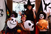 Preparing for Halloween. A young female teacher with her younger students dress up in a Halloween costume. Kids in creative carnival costumes ready for  Halloween party