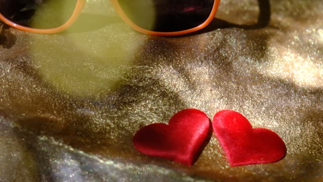 Close up trendy sunglasses on the golden sandy beach podium and two red heart. Honeymoon, travel, summer vacations concept