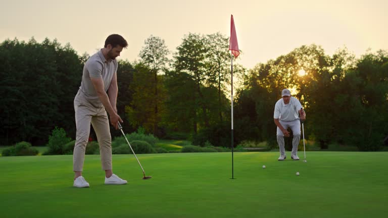 Golfers team hitting ball on sunset field course. Two players missing golf shot.