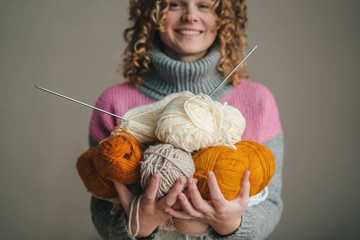 Curly-haired woman holding knitting yarn and needles on color background. Hobbies, leisure and needlework.