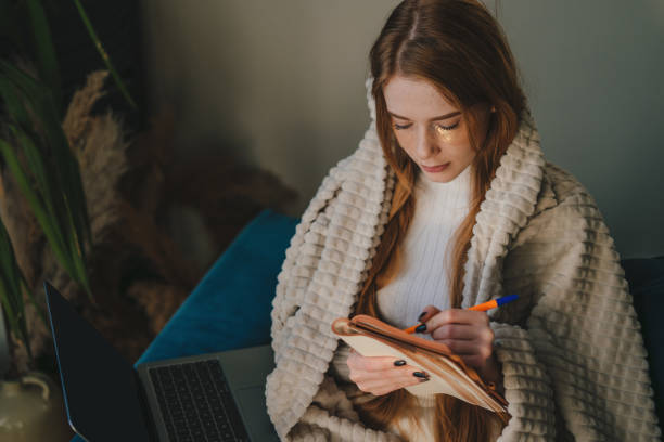 istock Ginger woman writing in her notebook while relaxing on the sofa. Self love, self care. Spend free spare time in living room indoors. People lounge concept. 1585835962