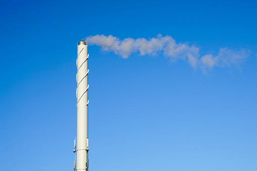 A tall white smoking chimney on a blue sky background, white steam smokes from the chimney