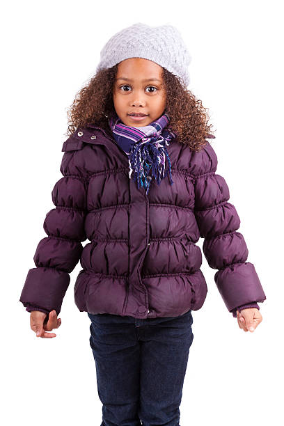 Little girl bundled up in a hat and purple coat on white stock photo