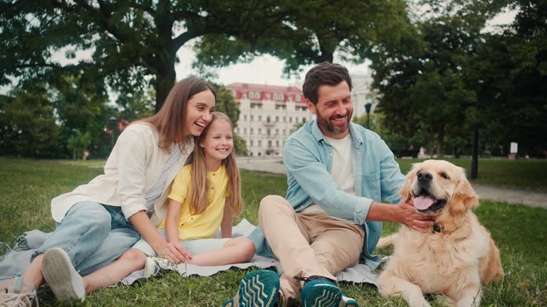 Parents and little girl with dog rest on mat on grassy lawn