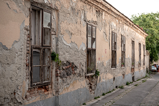 Exterior of aged abandoned building with crumbling stone walls and small windows located on street of small town