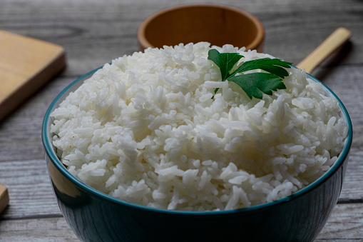 White rice in a green bowl.\nThere are two wooden bowls, some wooden spoons, chopping boards. All on a rustic gray table.