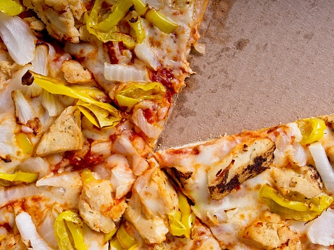 One slice gone out of box, a concept of a serving slice of pizza. Cardboard behind pizza slice can be used for copy. Pizza of chicken, roasted onion, and banana peppers.