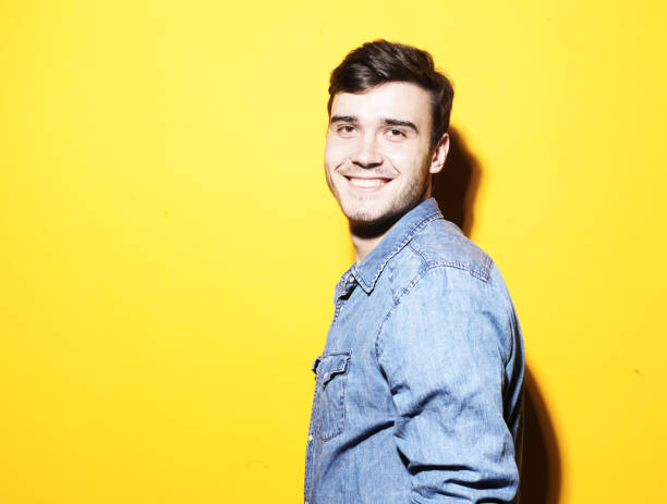 istock Smiling handsome male model in a denim jacket on a yellow background. 1586036850