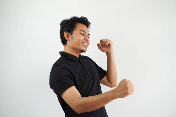joven asiático feliz bailando y divirtiéndose vistiendo una camiseta polo negra aislada sobre fondo blanco - menari fotografías e imágenes de stock