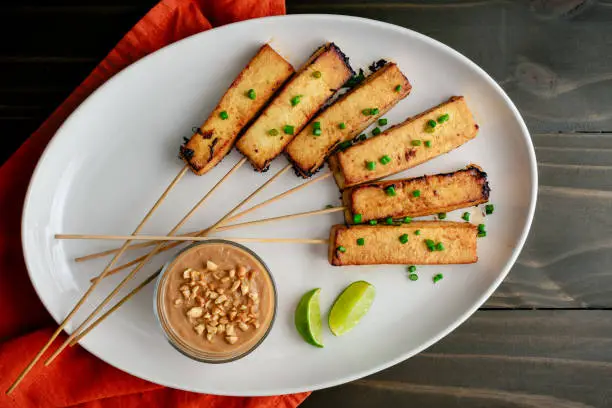 Marinated tofu served on bamboo skewers with peanut sauce and lime wedges