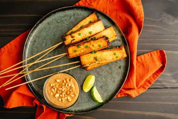 Marinated tofu served on bamboo skewers with peanut sauce and lime wedges