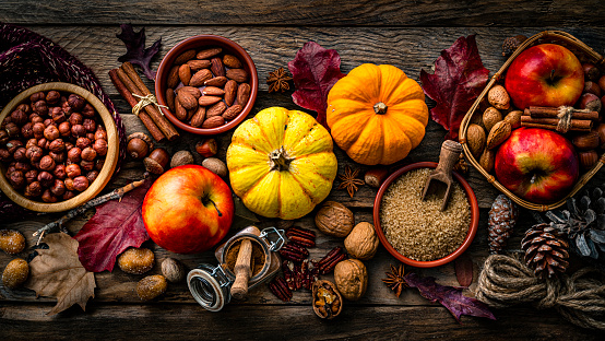 Autumn fruit (butternut squash, plum, pear, walnut, cinnamon) in a wicker basket on a rustic wooden background with dry leaves. Copy space. Top table view. Thanksgiving day, fall harvesting concept.