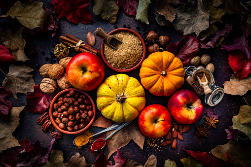 Autumn decorative pumpkins with apples, spices, nuts and fall leaves on dark background. Thanksgiving or Halloween holiday