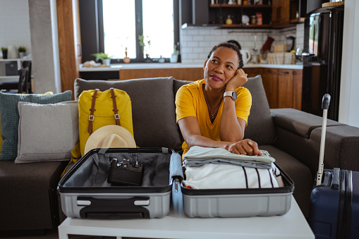 Pensive woman daydreaming about vacation. In front of her is packed suitcase